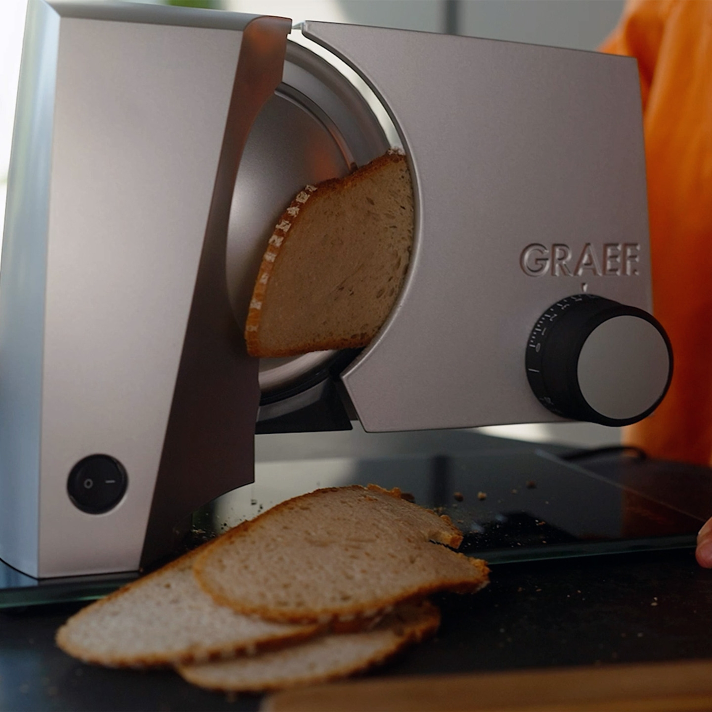 Ein Graef Brotschneidemaschine schneidet Brot. Mehrere Brotscheiben liegen daneben.