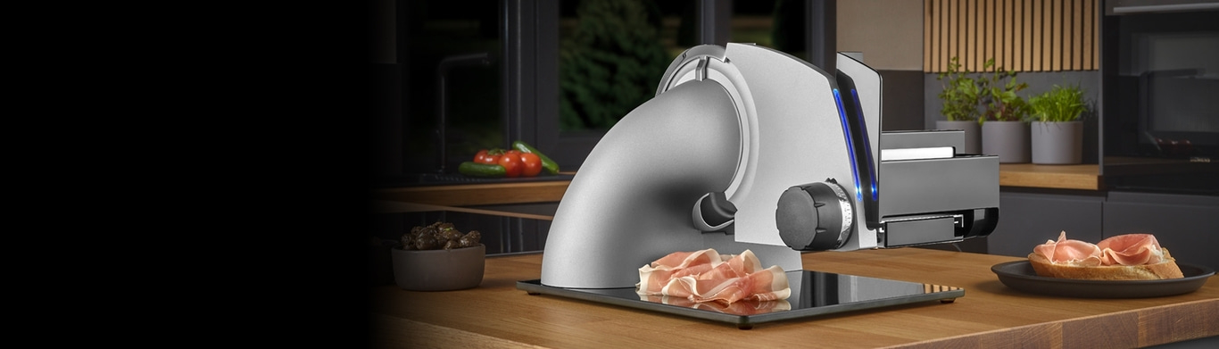 Elektrische Aufschnittmaschine mit Schinken auf einem Brotlaib in einer Küche.
