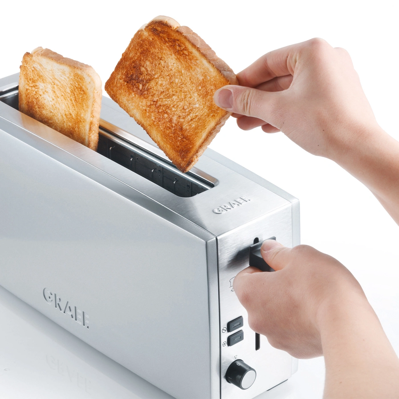 A person removing toast from a toaster. The toaster is silver and has buttons.