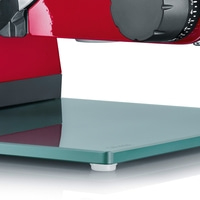 Close-up of a red meat slicer with a glass plate and adjustment dial.