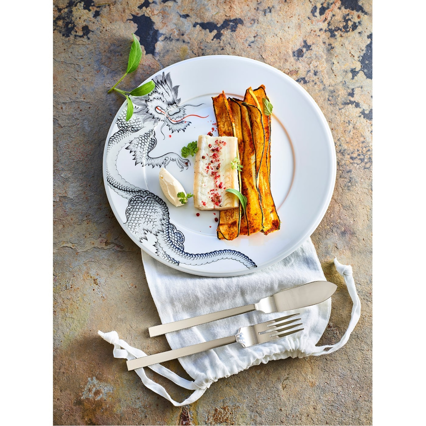 Plate of food, cutlery, napkin on stone. Delicious meal, well presented.