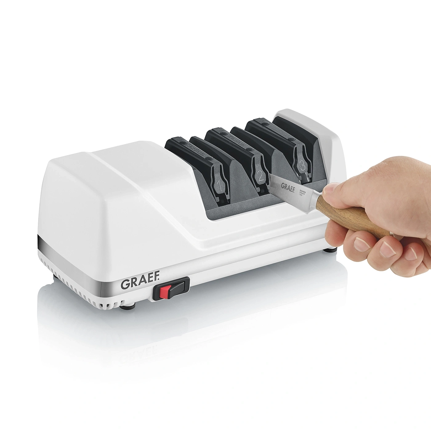 A white electric knife sharpener by Graef with a knife being inserted by a hand.