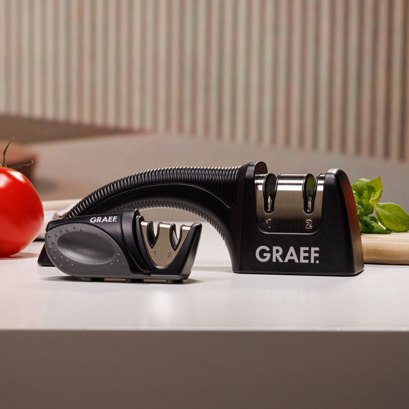 Black knife sharpener with GRAEF logo on white table with tomato and basil.