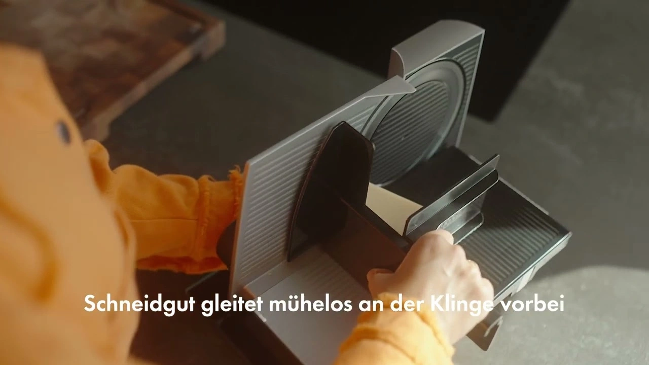 Close-up of a person operating an electric slicer with text in the image.