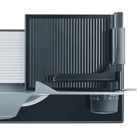 Close-up of an electric food slicer with adjustable carriage and scale.