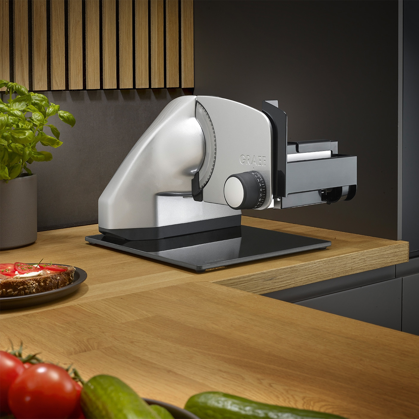 Graef Allesschneider auf Holztisch mit Gemüse und Brot im Vordergrund