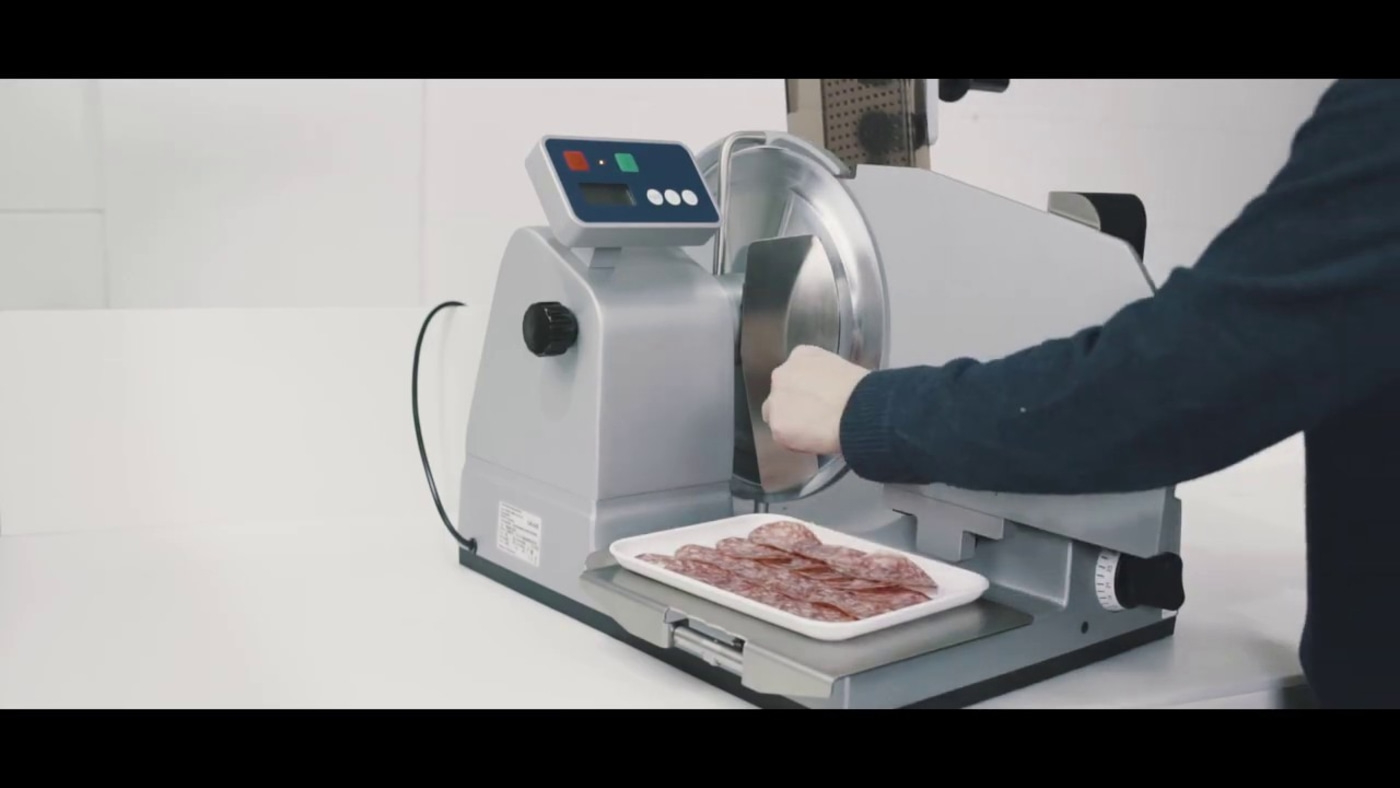 Fleischschneidemaschine schneidet Salami. Person bedient die Maschine. Auf Tablett liegen Scheiben.