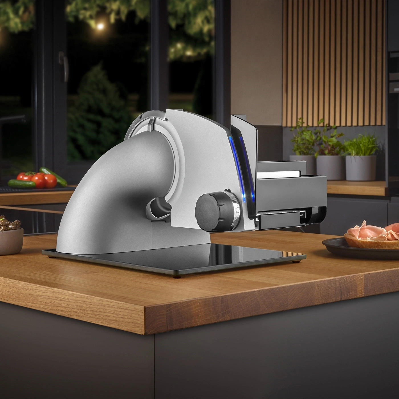 Electric slicer on wooden table in kitchen with food and plants