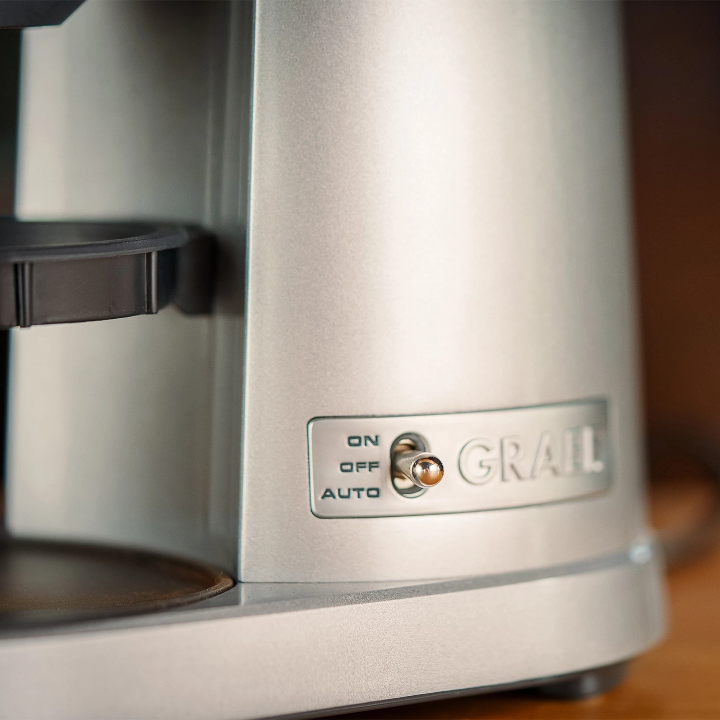 A close-up photo of a silver coffee maker with a switch and the name GRAIL.