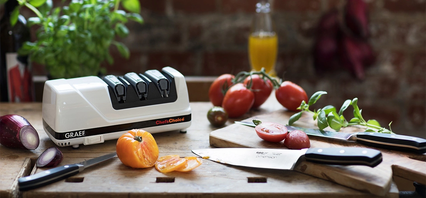 Kitchen scene with tomatoes, knives, sharpener, and vegetables on wooden surface