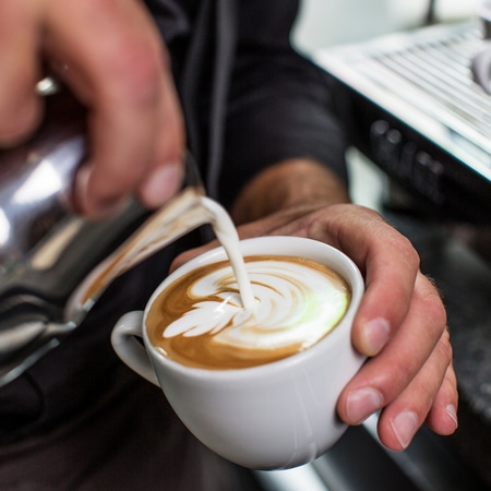 Kaffee mit Latte Art, der in einer weißen Tasse serviert wird, wird gegossen.
