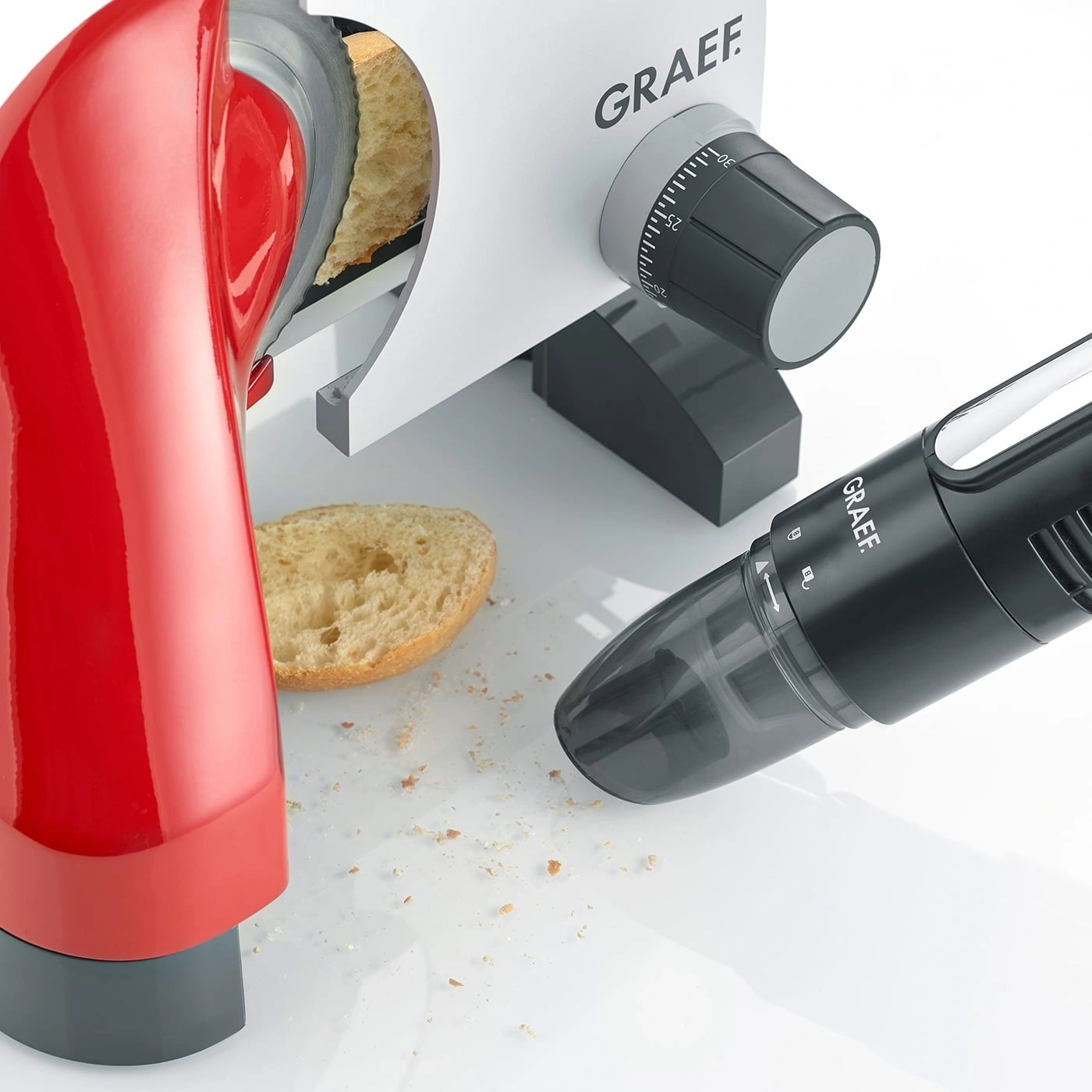 Red bread slicer with black vacuum cleaner and bread slice on white surface.