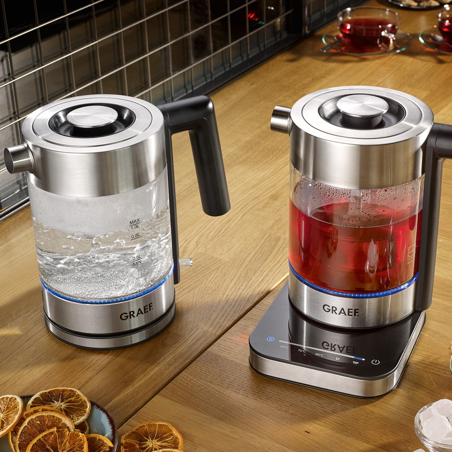 Zwei elektrische Wasserkocher auf einem Holztisch mit Tee und Dekoration.