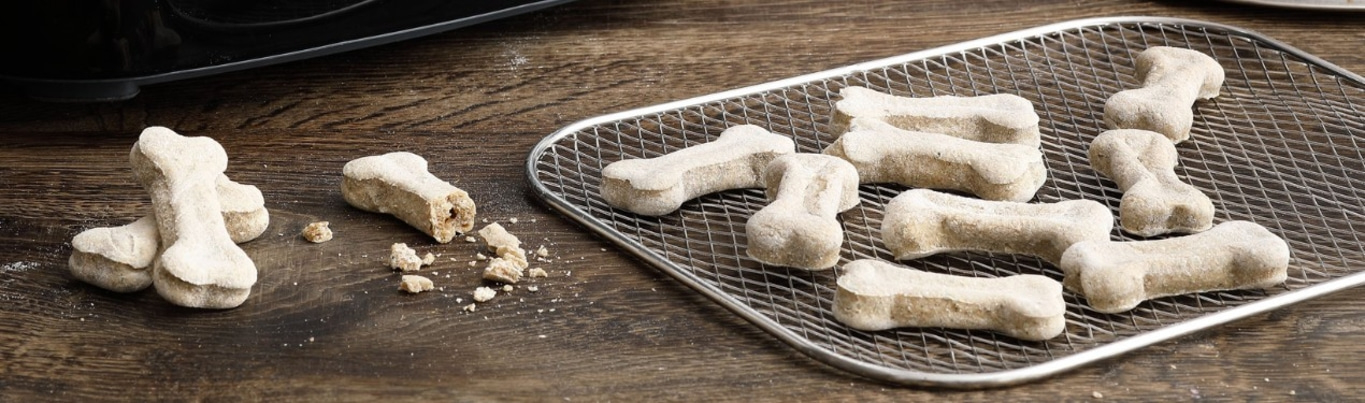 Hunde-Kekse in Knochenform auf einem Holzbrett und Gitter