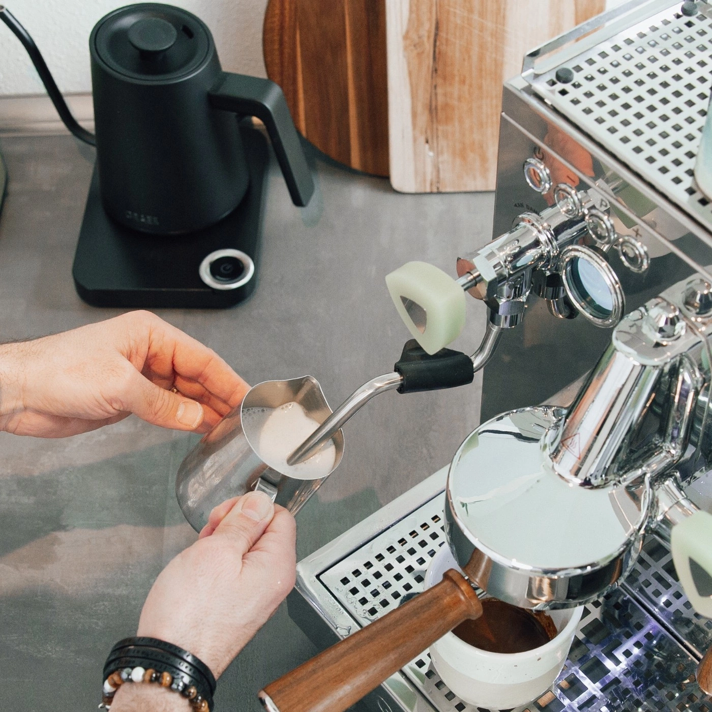 Person preparing coffee, frothing milk, espresso machine, kettle, hands, coffee cup