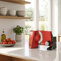 A red Graef food slicer sits on a kitchen counter next to tomatoes.