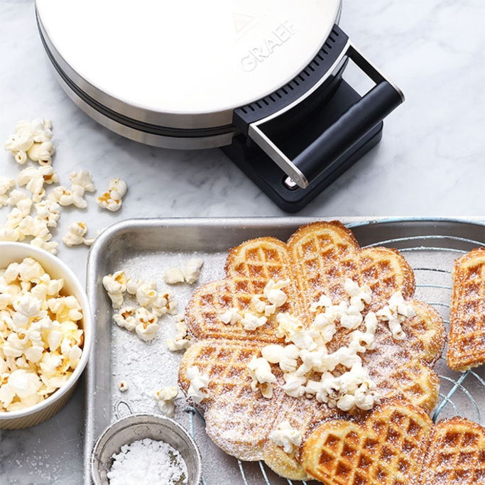 Waffeleisen mit Waffeln, Popcorn und Puderzucker auf einem Tablett