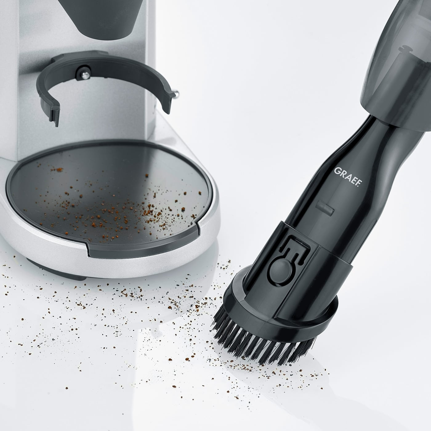 Kaffeemühle und Staubsauger mit Bürste reinigen Kaffeepulver auf weißem Untergrund.