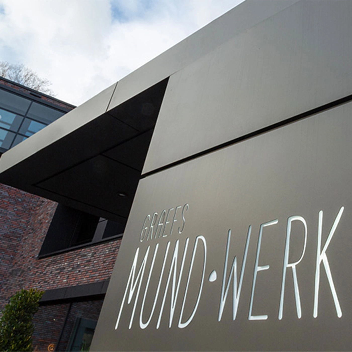 Gebäude mit Schriftzug 'Graefs Mund-Werk' und modernem Design, Himmel