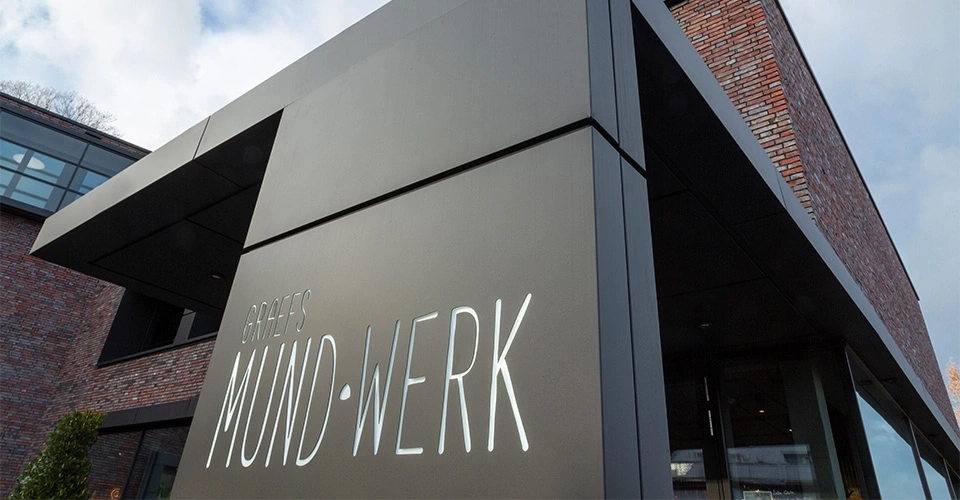 Gebäude mit Schild 'Graefs Mund-Werk' und Backsteinmauer im Hintergrund.