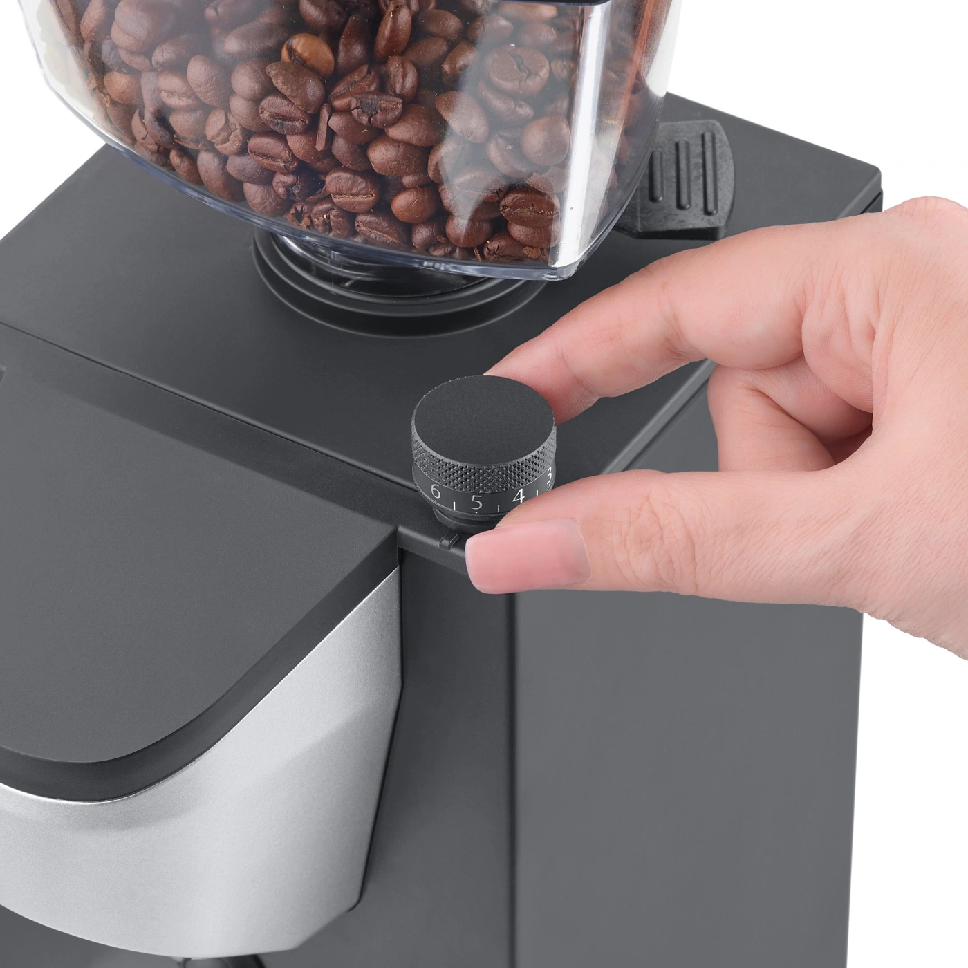 Hand turning a black knob on a coffee grinder with coffee beans in it