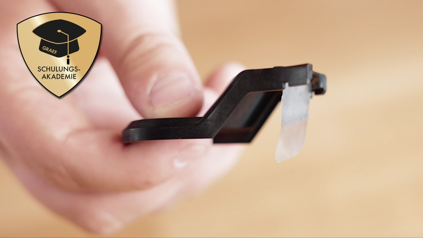 Black object with logo held by person against brown background, with a logo.