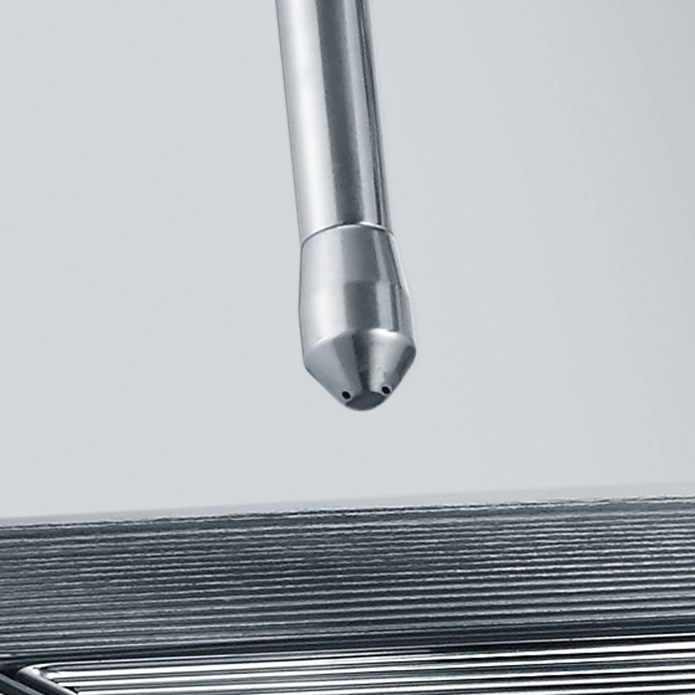 Metal pipe with nozzle pointing at a series of metal plates, close up