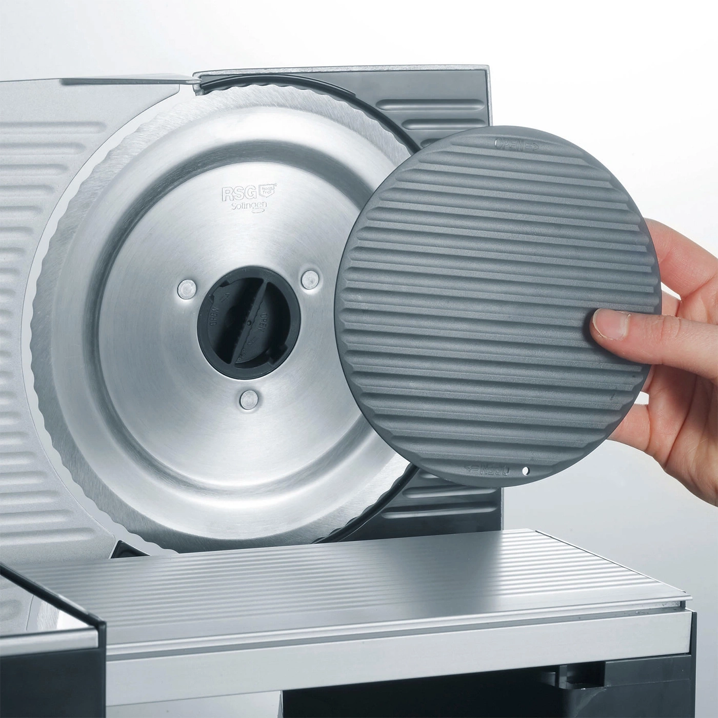 Close-up of a meat slicer with a protective cover held by a hand