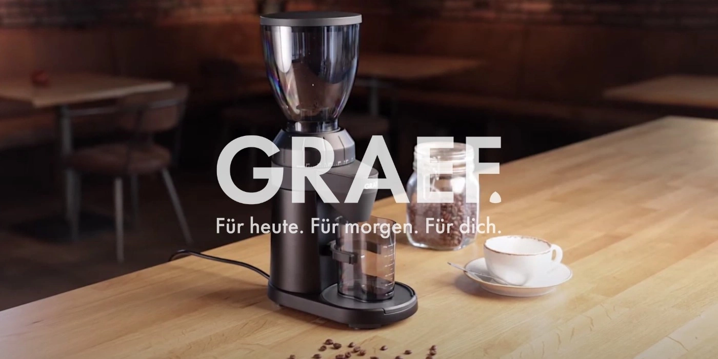 Coffee grinder with coffee beans and cup on a wooden table. GRAEF.