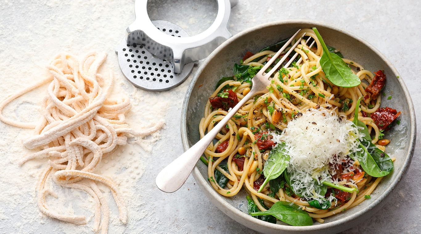 Pasta-Gericht mit Tomaten, Spinat und Käse, serviert mit einer Gabel.