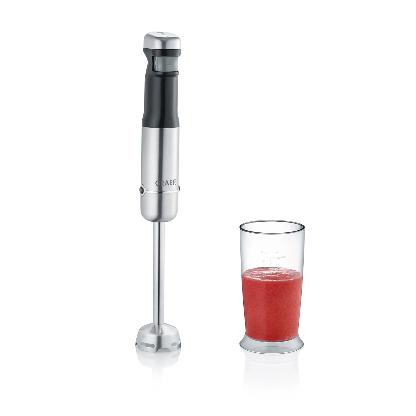 Immersion blender with glass of red smoothie on white background.