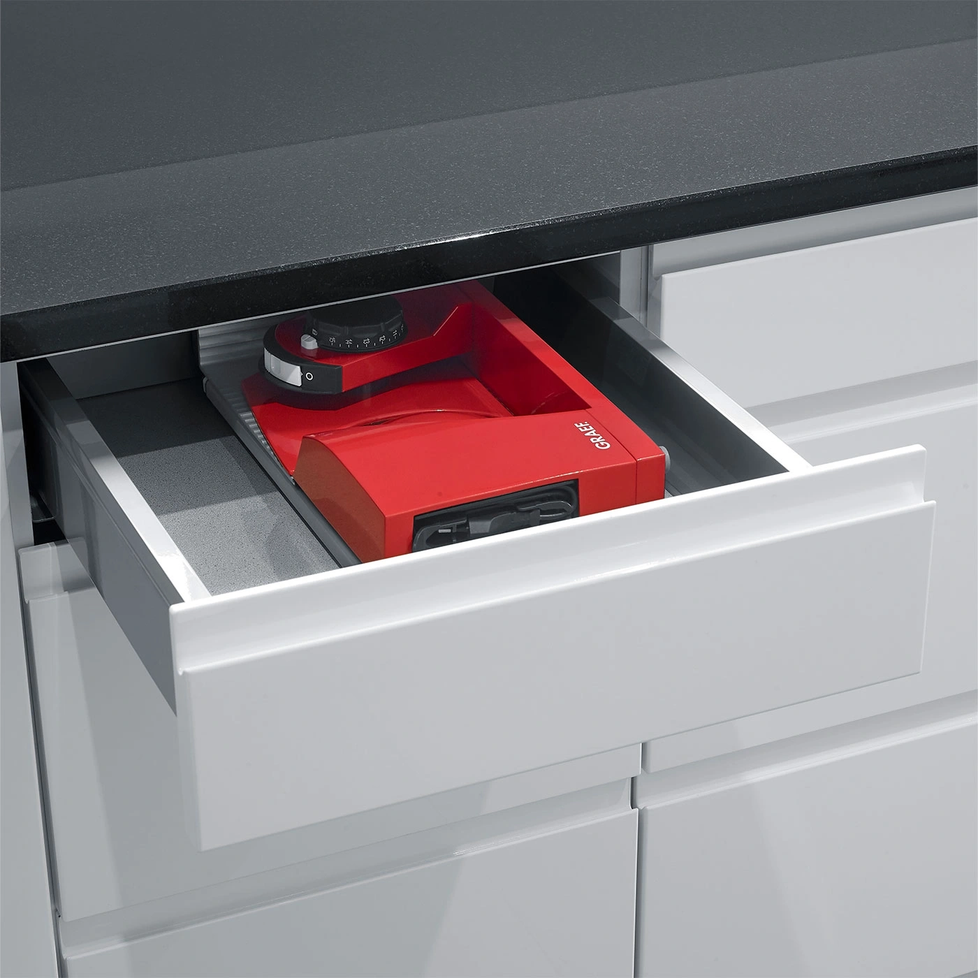 Red kitchen appliance in a drawer. Black countertop and white cabinets.