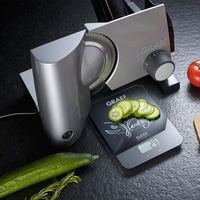 Graef slicer with cucumber slices and scale on a black surface.