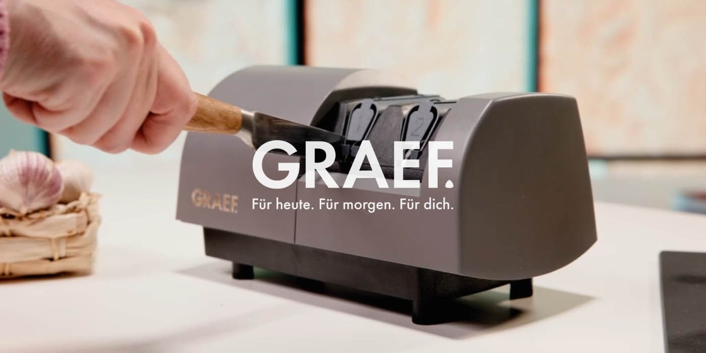 Messer wird in einem GRAEF-Messerschärfer geschärft, mit Knoblauch im Hintergrund.