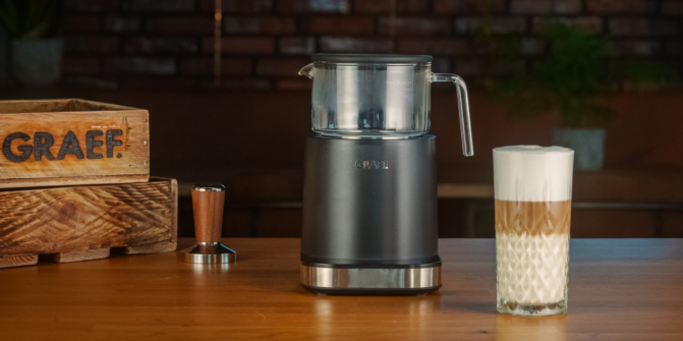Kaffeemaschine mit Glasbehälter und Latte Macchiato auf einem Holztisch