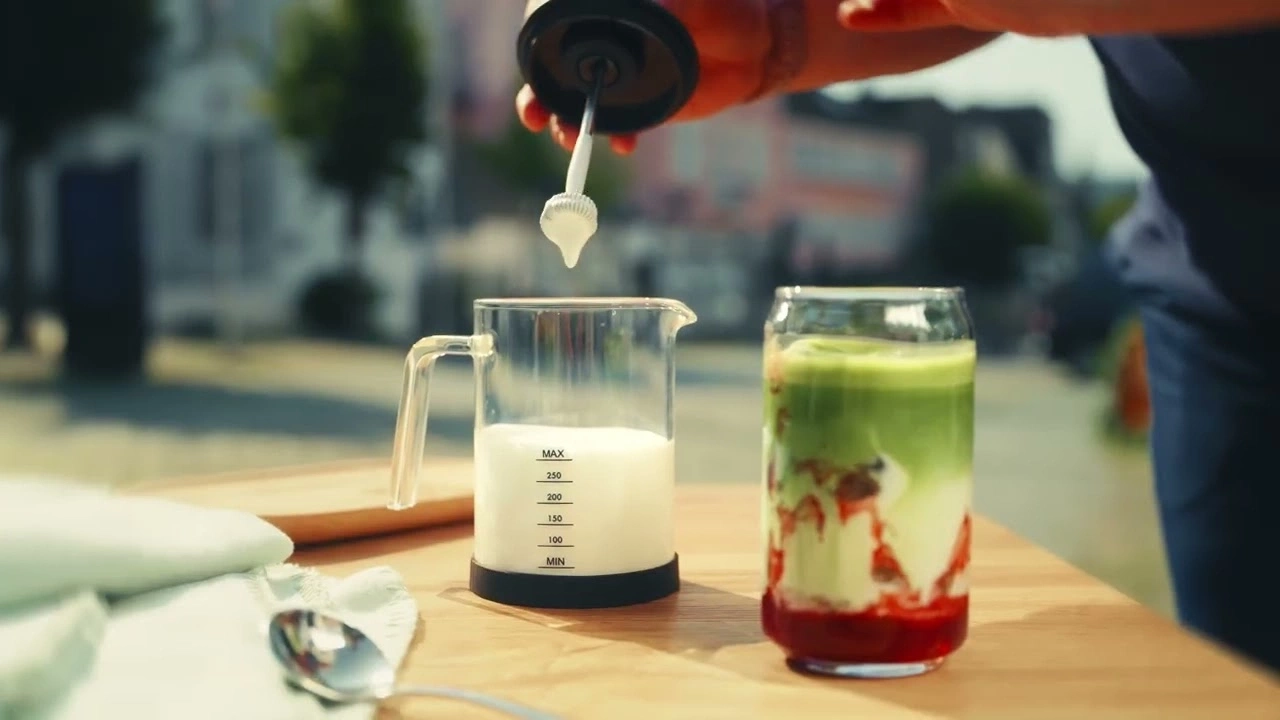 Person bereitet Getränk zu, Milch wird in ein Glas gegossen, Matcha-Getränk